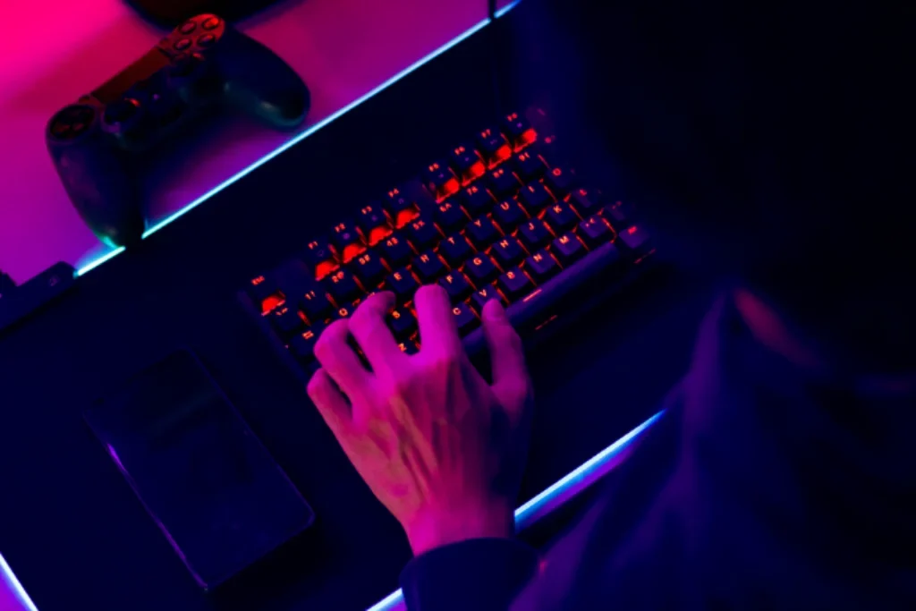 Uma pessoa com a mão em em cima de um teclado gamer onde contém um mouse pad gamer com luzes RGB.