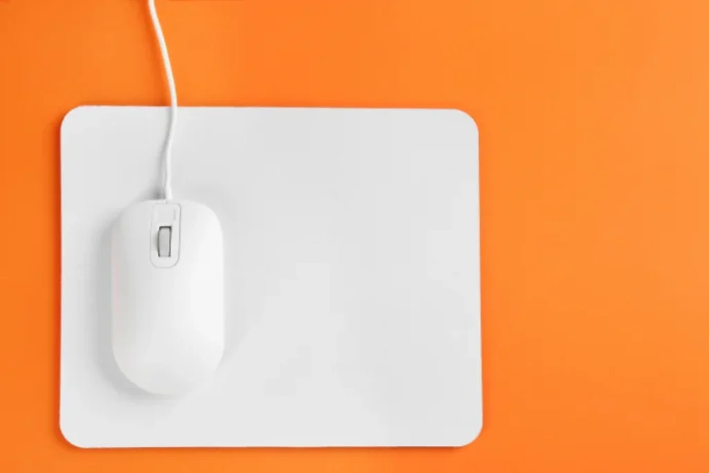 Um mouse branco em cima de um mouse pad branco em um fundo na cor laranja.
